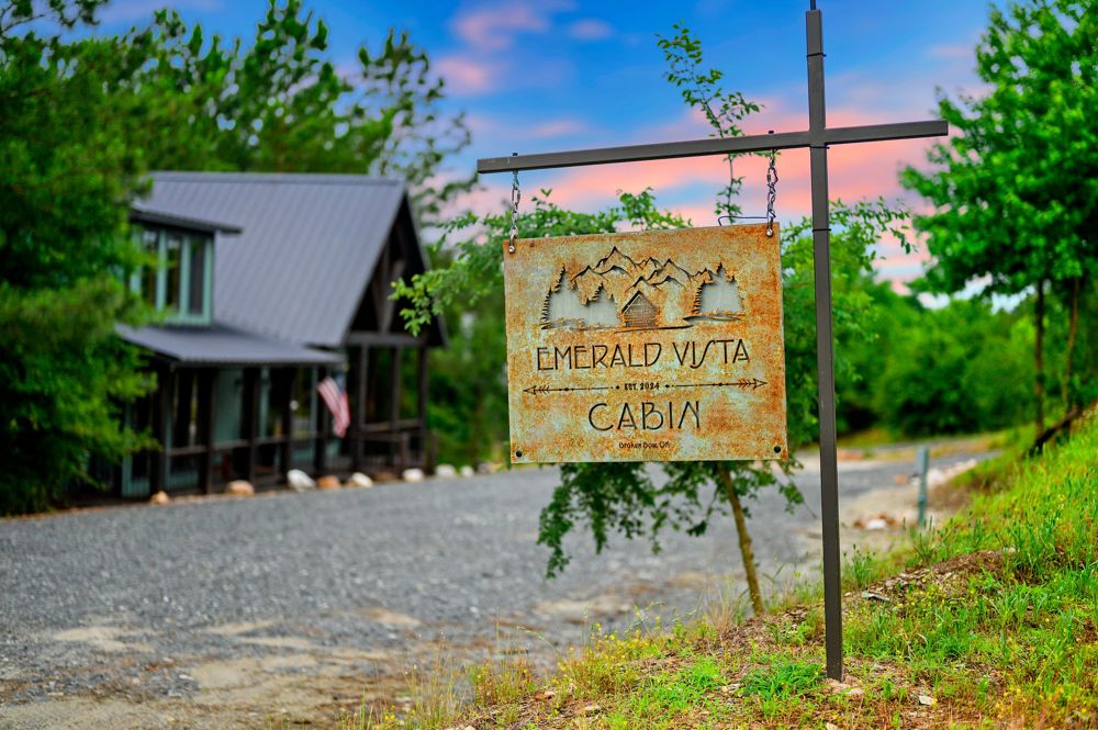 The Emerald Vista Cabin sign by the drive, the cabin behind it at dusk